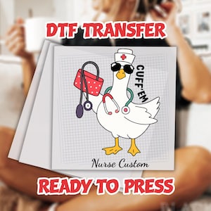 May include: DTF transfer featuring a cartoon goose dressed as a nurse, wearing sunglasses and a nurse's hat with a red cross. The goose holds a stethoscope and a red polka-dot bag. Text includes "CUFF'EM", "Nurse Custom", and "READY TO PRESS".
