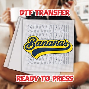 May include: A white sheet of DTF transfer paper with the words "SAVANNAH Bananas" in a navy and yellow design. The words "DTF TRANSFER" and "READY TO PRESS" are in red text.