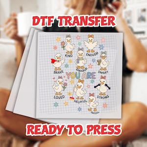 May include: A DTF transfer sheet featuring cartoon ducks with various accessories and the words "Brave," "Kind," "Enough," "Unique," "Smart," "Loved," "Helpful," "Strong," and "Grateful." The phrase "You Are" is also present. The words "DTF TRANSFER" and "READY TO PRESS" are also visible.