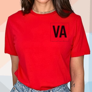May include: A bright red t-shirt with short sleeves. The shirt features the letters "VA" inside a black square on the upper left chest, with the words "social content" below. The model is wearing blue denim shorts.