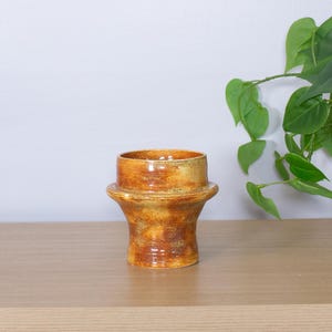 May include: A handcrafted ceramic vase with a unique, textured design. The vase features a warm color palette of orange, brown, and yellow, with a glossy finish. The vase is a decorative item for the home.