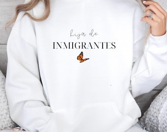 May include: White hoodie with the text "hija de INMIGRANTES" and a small orange butterfly graphic.