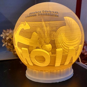 Könnte beinhalten: Eine kugelförmige, beleuchtete Lampe mit warmem gelbem Licht. Die Oberfläche zeigt ein Reliefdesign mit einem Anker, einer Muschel und dem Wort MOIN. Der Text oben lautet Klefana Oderbruch Whatsapp 015225302084. Die Lampe steht auf einem weißen Sockel.