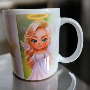 May include: White ceramic mug featuring a cartoon angel with blonde hair, blue eyes, and a halo. The angel wears a white dress and has small white wings. The mug has a curved handle and is likely used for hot beverages.