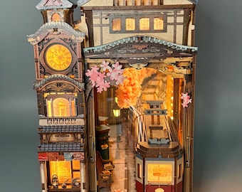 May include: A detailed wooden model of a Japanese train station featuring a clock tower, a train, and cherry blossoms. The model is illuminated with warm lighting, creating a cozy atmosphere. The base of the model reads "ECHO PLATFORM".