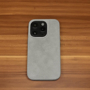 May include: A silver phone case with a textured surface. The case has a camera lens cutout with three black circles.