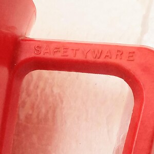 May include: Close-up of a red plastic pitcher with the word "SAFETYWARE" embossed on the handle.