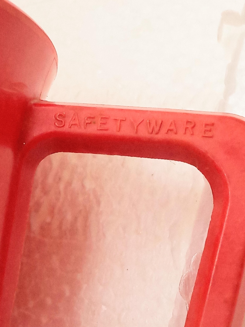 May include: Close-up of a red plastic pitcher with the word "SAFETYWARE" embossed on the handle.