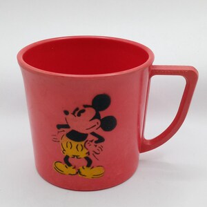 May include: A red plastic cup with a black and yellow image of Mickey Mouse.