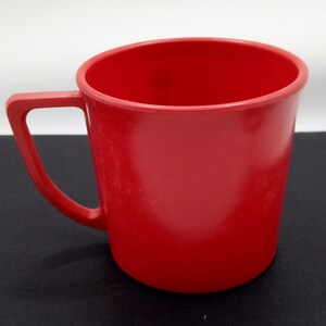 May include: A solid red plastic mug with a handle. The mug is a simple design with no embellishments.