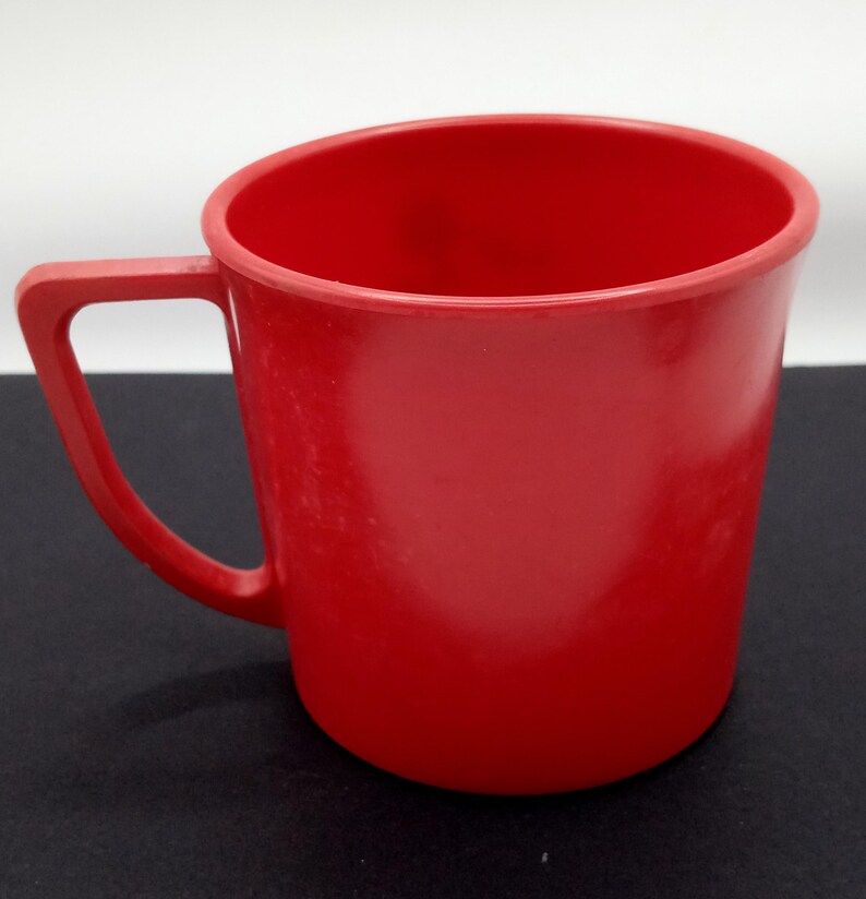 May include: A solid red plastic mug with a handle. The mug is a simple design with no embellishments.