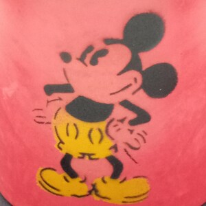 May include: Red ceramic mug with a black silhouette of Mickey Mouse. Mickey is wearing yellow shorts and black shoes.