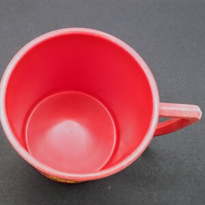May include: A red plastic mug with a handle. The mug is empty and has a smooth surface.