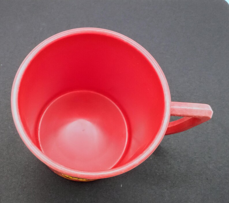 May include: A red plastic mug with a handle. The mug is empty and has a smooth surface.