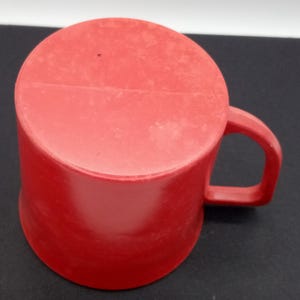 May include: A red plastic mug with a handle. The mug is slightly chipped on the top edge.