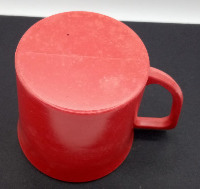 May include: A red plastic mug with a handle. The mug is slightly chipped on the top edge.