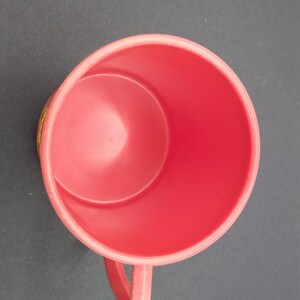 May include: A red plastic mug with a handle. The mug is empty and has a smooth surface.