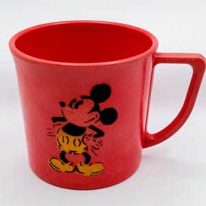 May include: Red plastic cup with a Mickey Mouse design. The cup has a handle and is perfect for kids.