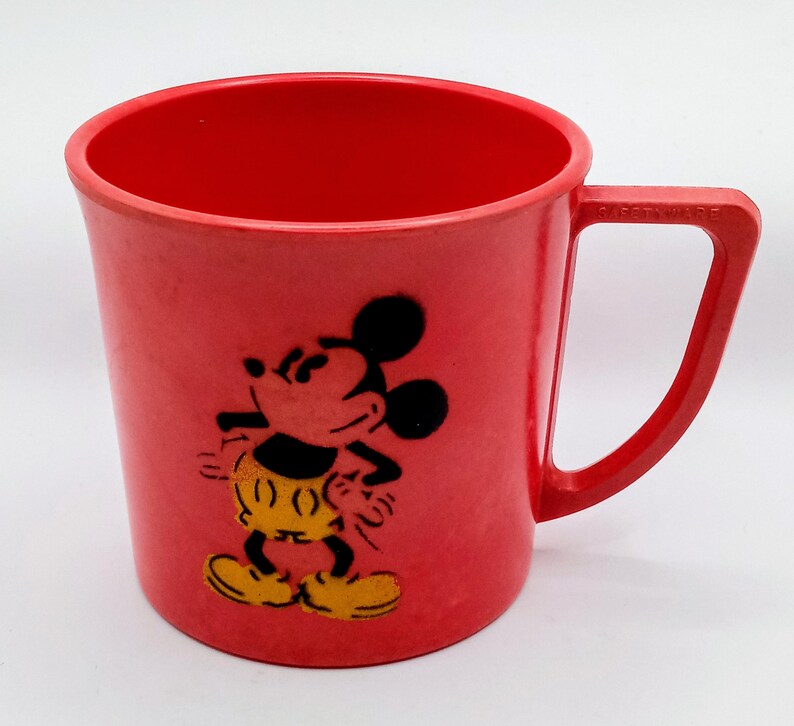 May include: Red plastic cup with a Mickey Mouse design. The cup has a handle and is perfect for kids.
