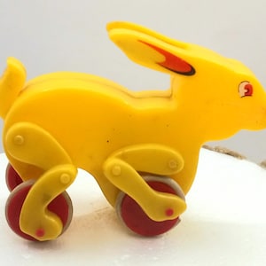 May include: A vintage yellow toy rabbit with red and yellow wheels. The rabbit has red accents on its ears and nose. The toy is made of plastic and has a classic design, perfect for collectors or as a decorative item.