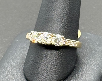 May include: A gold band ring with three round diamonds and smaller diamonds set in the band.