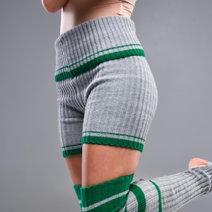 May include: Gray ribbed knit shorts and leg warmers with green stripes. The shorts have a high waistband and green trim at the hem. The leg warmers extend from the ankle to the mid-thigh, also with green stripes.