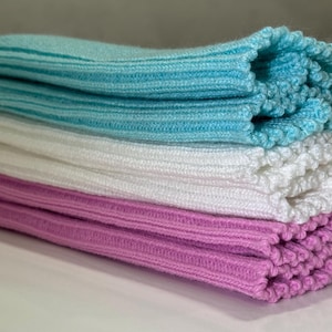 May include: A stack of folded knitwear in shades of blue, white, and pink. The top layer is a light blue, followed by white, and then a vibrant pink. The ribbed texture is visible, suggesting a soft, comfortable material.