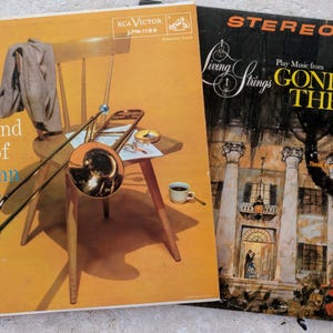May include: Two vintage vinyl record album covers. The left cover is yellow with a trombone, a chair, and text reading The Sound of Glenn Miller. The right cover is black with an illustration of a mansion and text reading Living Strings Play Music from Gone With The Wind and Other Motion Pictures.