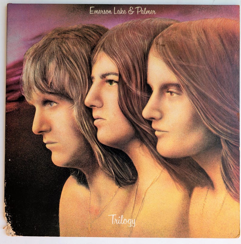 May include: Album cover art featuring three side profiles of individuals with long hair, set against a purple and brown background. The text "Emerson Lake & Palmer" is at the top, and "Trilogy" is at the bottom.