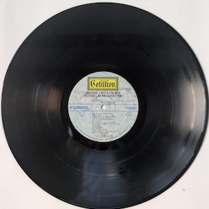 May include: A black vinyl record with a white and blue label. The label features the text "Cotillion" and "EMERSON, LAKE & PALMER PICTURES AT AN EXHIBITION". The record is a stereo recording.