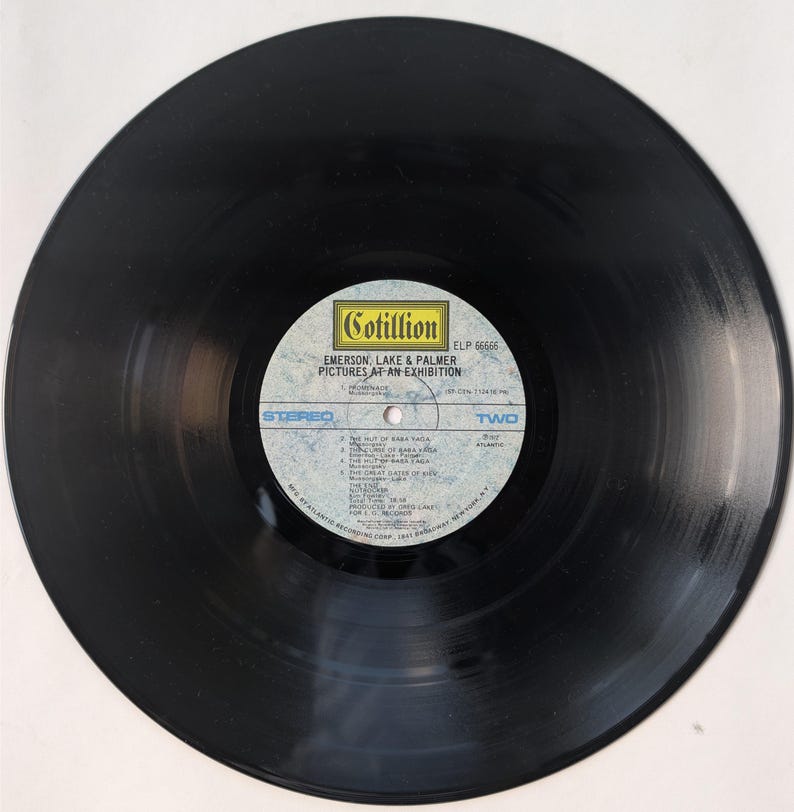 May include: A black vinyl record with a white and blue label. The label features the text "Cotillion" and "EMERSON, LAKE & PALMER PICTURES AT AN EXHIBITION". The record is a stereo recording.