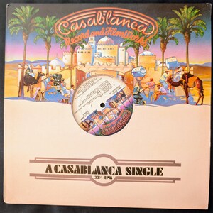 May include: A vintage Casablanca Records album cover with a desert scene featuring camels, palm trees, and a city. The album cover has the text "Casablanca Record and Filmworks" and "A Casablanca Single". A vinyl record is in the center.