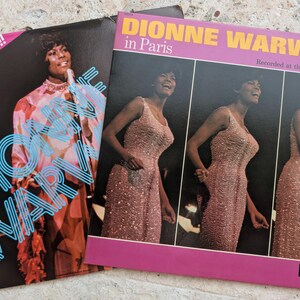 May include: Two vintage vinyl record album covers featuring Dionne Warwick. The left cover shows a portrait with the text "Dionne Warwick" and "2 Record Set!!!". The right cover displays three images of the artist in a pink gown with the text "Dionne Warwick in Paris" and "Recorded at the Olympia Theater".