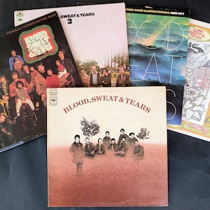 May include: A collection of vintage vinyl records featuring album covers with various designs and text. The albums include "Blood, Sweat & Tears" and "Child's Father to the Man". The covers display images of people and artistic graphics.