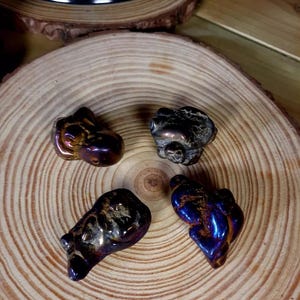 May include: Four small, iridescent blue and brown, irregularly shaped, polished stones on a wooden surface.