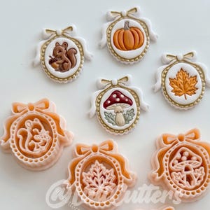 Op de afbeelding: Een verzameling van zeven ovale koekjesvormen en bijpassende koekjes met herfstthema's. De ontwerpen bevatten een eekhoorn met een eikel, een pompoen, een esdoornblad en een paddenstoel, allemaal omlijst door een decoratieve strik en rand.