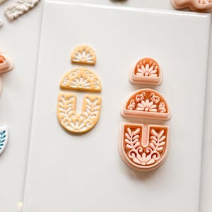 Pode incluir: Vista aérea de vários cortadores de argila polimérica em uma variedade de formas e cores. Os cortadores incluem desenhos florais e de folhas, bem como formas de cactos. Os cortadores são em tons de amarelo, pêssego, verde e branco.