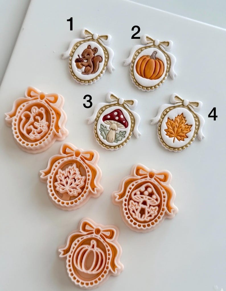 May include: A collection of oval-shaped cookie cutters and corresponding embossed cookies featuring autumn themes. The designs include a squirrel with an acorn, a pumpkin, a mushroom, and a maple leaf, all framed by a decorative bow and border.