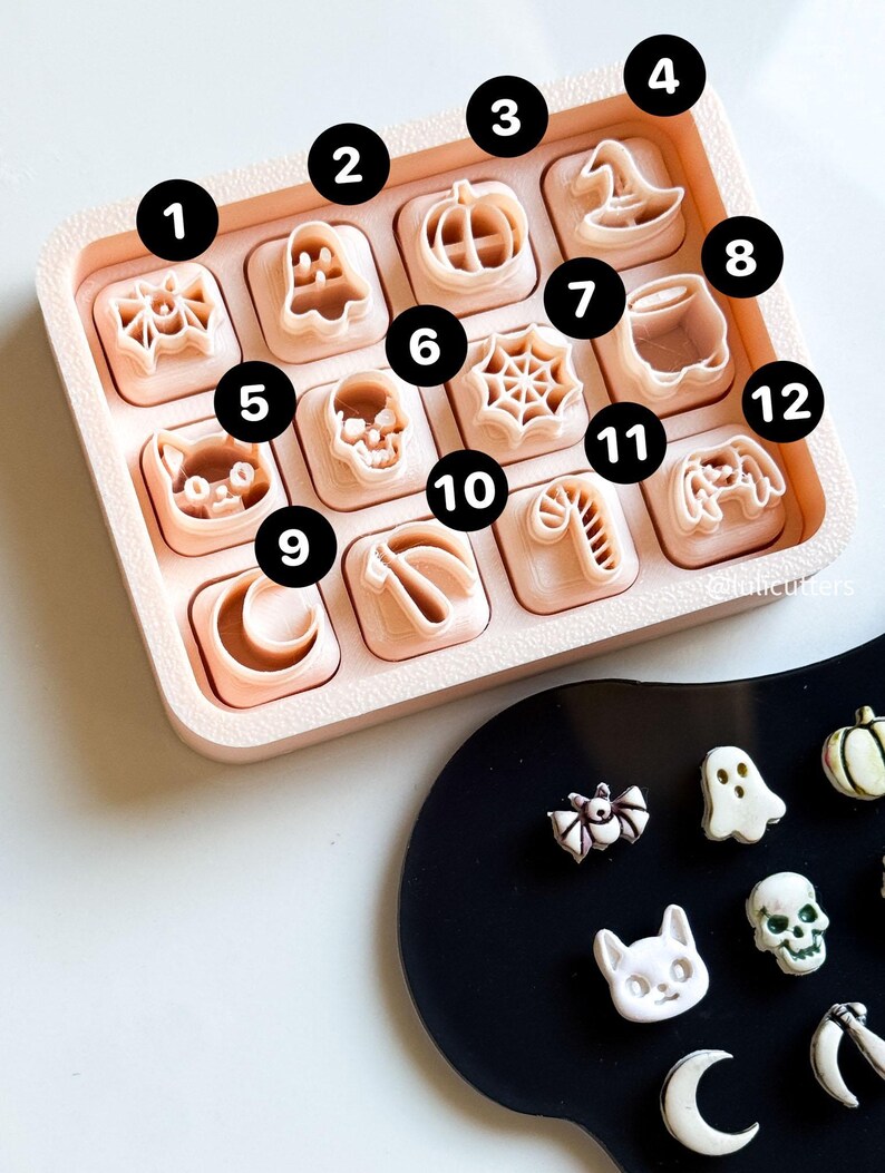 May include: A collection of Halloween-themed cookie cutters in a light pink tray. The cutters include shapes like a spider, ghost, pumpkin, witch's hat, cat, skull, spiderweb, cauldron, crescent moon, candy cane, and a video game controller.