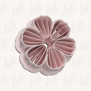 Puede incluir: Un cortador de galletas en forma de flor rosa claro. El cortador tiene seis p&eacute;talos con crestas detalladas y un borde redondeado. El dise&ntilde;o es una sola pieza de pl&aacute;stico, con el nombre de la marca "Luli" repetido en el fondo.