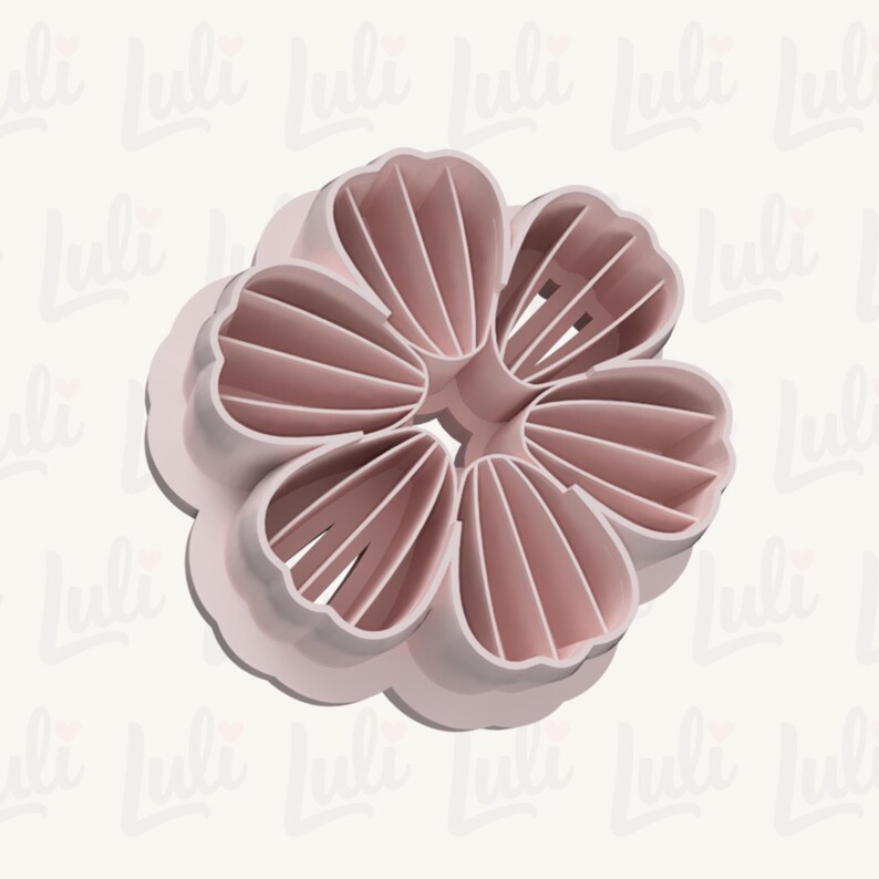 Puede incluir: Un cortador de galletas en forma de flor rosa claro. El cortador tiene seis p&eacute;talos con crestas detalladas y un borde redondeado. El dise&ntilde;o es una sola pieza de pl&aacute;stico, con el nombre de la marca "Luli" repetido en el fondo.