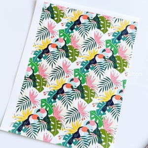 May include: A seamless pattern featuring toucans with orange beaks and black bodies perched on green and yellow tropical leaves. The background is white with pink flowers.