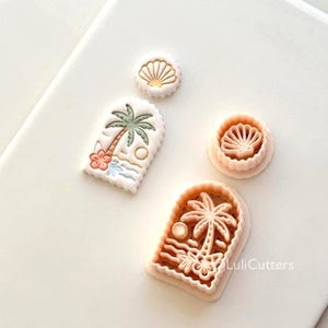 May include: A selection of cookie cutters featuring a palm tree, seashell, and beach design. The cutters are in pink, white, and green. One cutter has the text "LuliCutters".