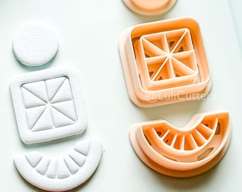 May include: A collection of light peach-colored and white cookie cutters in various shapes, including a circle, square with a geometric design, and a watermelon slice. The cutters are arranged on a white surface.