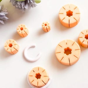 May include: A set of six orange silicone molds shaped like pineapples with a star-shaped center hole. The molds are arranged on a white surface.