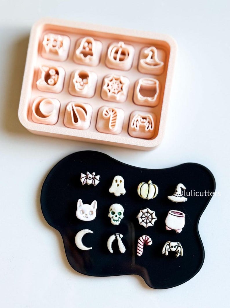 May include: A light pink tray with 12 Halloween-themed cookie cutters, including a ghost, pumpkin, and witch's hat. A black, irregularly shaped tray holds 12 decorated Halloween cookies, including a spider, skull, and candy cane.