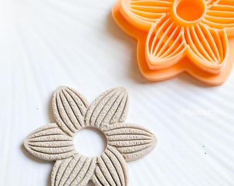 Peut inclure: Un emporte-pièce en forme de fleur de couleur brun clair avec une surface texturée et un trou circulaire au centre. L'emporte-pièce est fait d'argile polymère et est utilisé pour faire des biscuits.