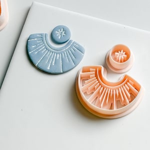Peut inclure: Deux emporte-pièces de boucles d'oreilles en pâte polymère. L'un est bleu clair avec un motif de soleil et un petit cercle avec une étoile. L'autre est de couleur pêche avec un motif de soleil et un petit cercle avec une étoile.