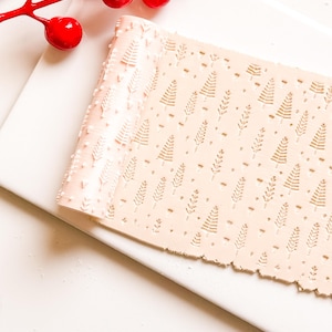May include: A light beige clay sheet with an embossed pattern of small Christmas trees and leaf sprigs. The clay is rolled out and has a textured edge. A red berry branch is in the upper left corner.