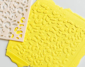 May include: A light beige stencil with an organic pattern is placed over a textured yellow surface. The yellow surface has a raised pattern that mirrors the stencil design. The image is a close-up shot, highlighting the textures and colors.